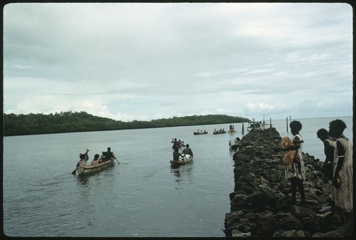 People at sea in canoes, and on rocky pier