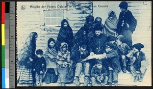 Women and children gathering around a missionary father in front of a wooden building, Canada, ca.1920-1940
