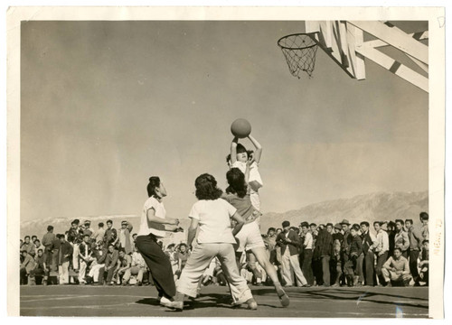 Photograph of four girls playing basketball with crowd watching at Manzanar