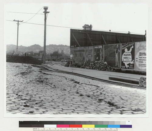Corner of 18th and Howard Streets [later South Van Ness Street]. [View northwest from 18th, toward Mission Dolores and Corona Heights. Shows damages cobbled street and burned Mission District.]
