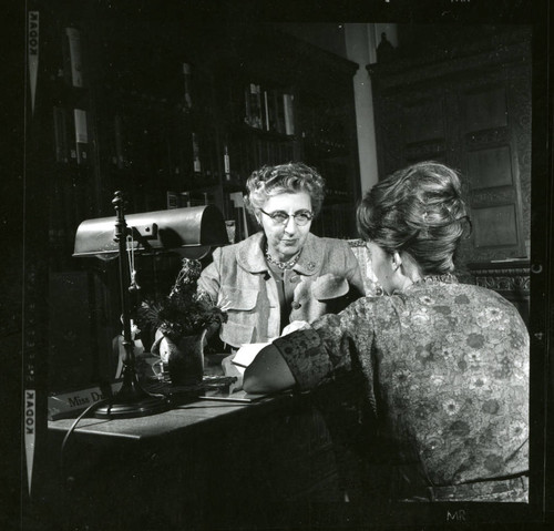 Dorothy Drake listens to the student librarian sitting by her desk, Scripps College