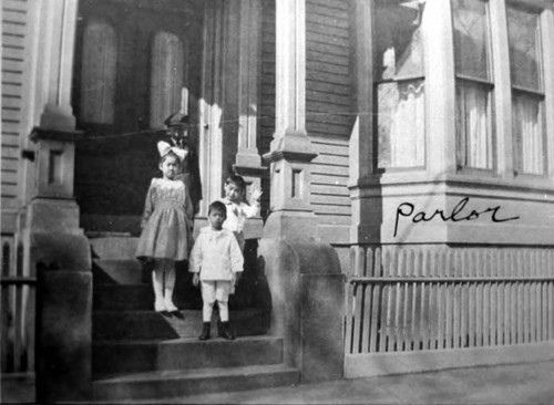 Man and three children on steps in front of the front door and the parlor