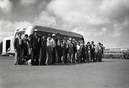 Mexican workers standing in front of bus. The bus, in background, is labeled Pacific Greyhound Line