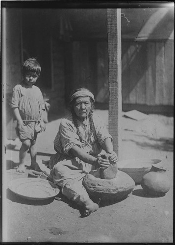 Paiute woman grinding meal on stone mortar (or metate), using stone pestle