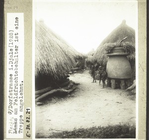 Dorfstrasse i. Djale (1928). Im Vordergrund ein Behälter für Feldfrüchte. Die Öffnung ist oben, man steigt mit einer Leiter hinauf. Diese Behälter werden gebaut wegen der Ratten, die über die obere Ausbuchtung nicht hinauskönnen. Im Fall eines Dorfbrandes bleiben die Früchte unversehrt