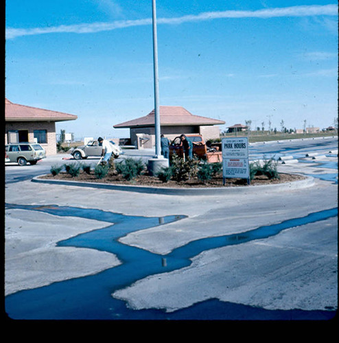 View of gardener, parking lot, and park hour sign at Apollo Park