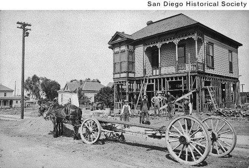 A horse-drawn lumber wagon and construction workers at a house under construction on Evans Street
