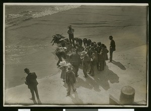 Men looking down into a fishing boat that has just landed in Newport Beach, ca.1910