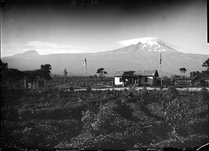 Small house and flag poles in front of Kilimanjaro, Tanzania, ca.1893-1920