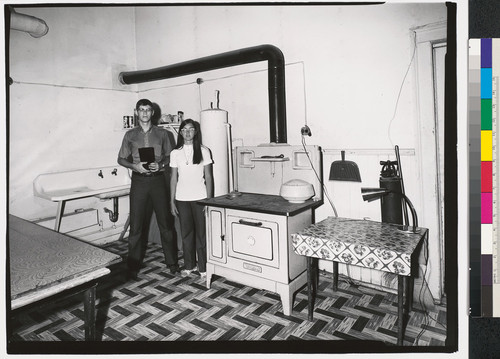 [Young man and woman standing next to stove and sink in kitchen.]