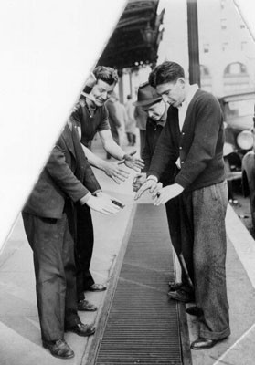 [Four men warming their hands over a grate in the sidewalk outside the Palace Hotel]