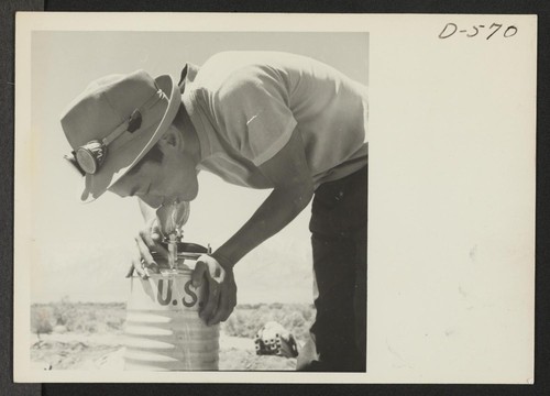 Masaro Takahashi, 19, evacuee farmer from Malibu Beach, takes a drink from a portable Army canteen on the farm at the relocation center. Photographer: Stewart, Francis Manzanar, California