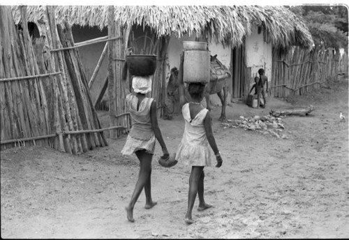 Two girls walk on the street and carry buckets on her head, San Basilio de Palenque, 1975