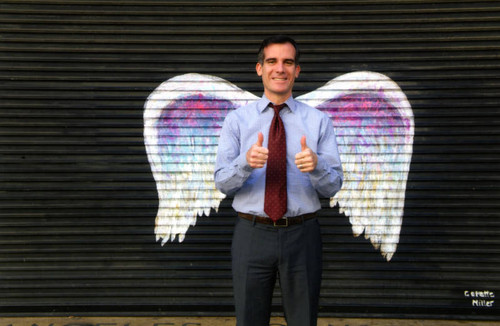 Mayor Eric Garcetti giving a "thumbs up" and posing in front of a mural depicting angel wings