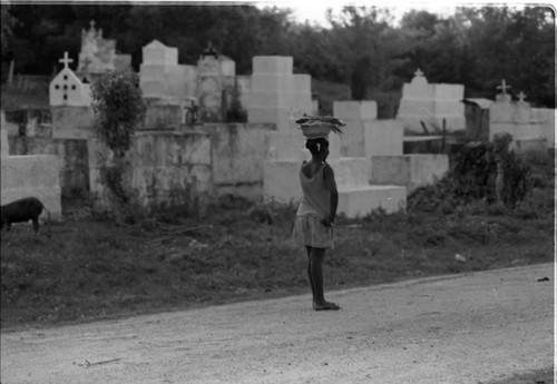 Woman with a bowl full of fish walks along a cemetery, San Basilio de Palenque, 1975