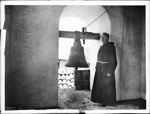 Father Superior Peter Wallischeck in the west tower standing beside the largest and oldest bell, Mission Santa Barbara, 1898