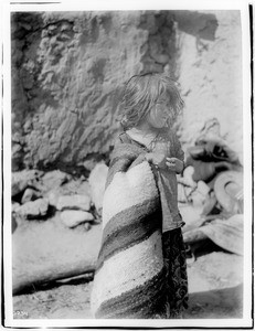 Young Navajo Indian girl standing in front of an adobe dwelling, ca.1900