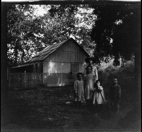 A group of five children standing in front of wooden house