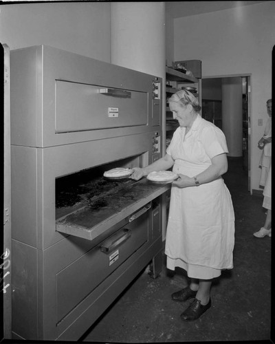 Woman taking pies out of baking oven in commercial kitchen