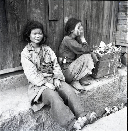Two young women sitting against a wall
