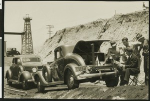 Men next to two automobiles in front of an oil well, ca.1930