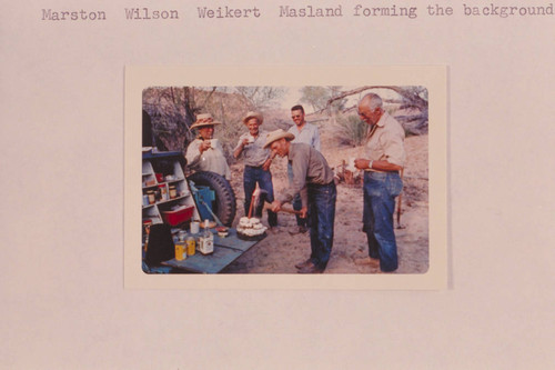 Art Ekker cutting his birthday cake with the proverbial axe; Bakers Ranch. Pictured are: Marston, Wilson, Weikert and Masland forming the background
