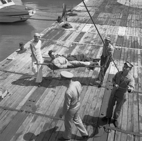 Sailors carrying a wounded man by stretcher accross a dock