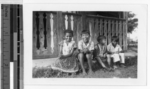 Four children sitting outdoors in front of a carved porch railing, Mexico, ca. 1948