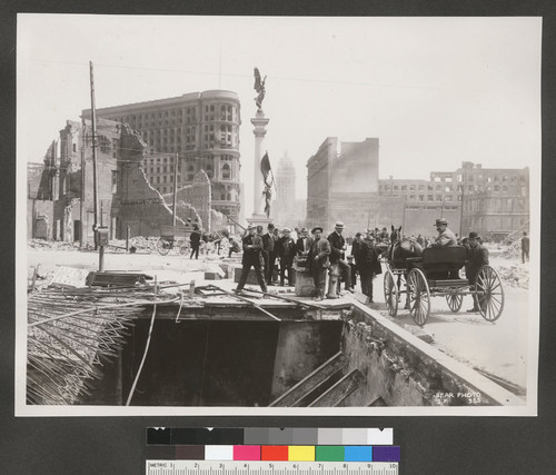 [Men posing at opening in ground. From Turk and Mason Sts. (?) at Market. Native Sons of the Golden West statue, center; Flood Building, Call Building and Emporium department store in background center.]