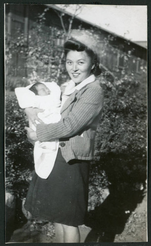 Photograph of a woman holding an infant in front of a building at Manzanar