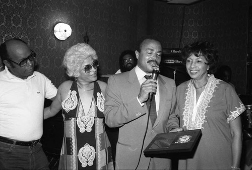 Alonzo Miller holding an award while posing with others at the Pied Piper nightclub, Los Angeles, 1983