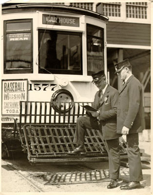 [Two streetcar conductors standing in front of a streetcar outside a carbarn]