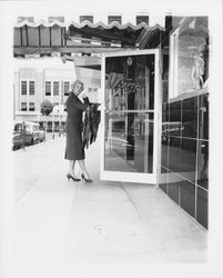 Model in a worsted wool skirt and jacket at the door of the Topaz Room where the "Dramatic Moods" fashion show will be held, Santa Rosa, California, 1959