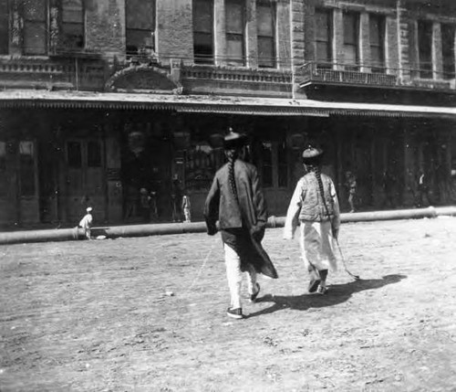 Two Chinese residents of the original Chinatown cross North Los Angeles Street toward the Garnier Building