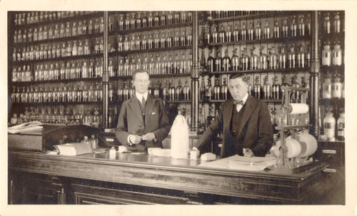 [Two men standing behind the counter at Broemmel's Pharmacy]