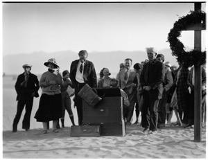 People gathered in front of a piano and cross for a funeral in the desert