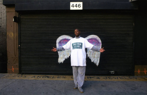Unidentified man with outstretched arms posing in front of a mural depicting angel wings