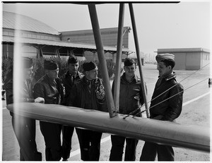 Group of six soldiers standing near the wing of a biplane