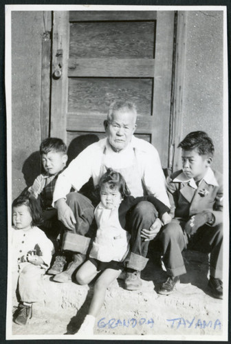 Photograph of Grandpa Tayama surrounded by four children in front of a door in Cow Creek Camp in Death Valley