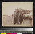 Three Indians, possibly Apache or Yuma, standing in front of wood pile, wearing blankets and head wraps