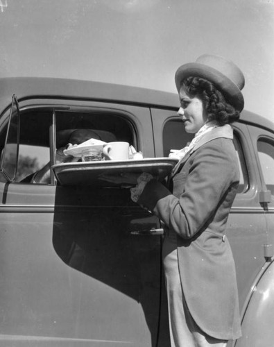 Carhop holding a tray next to car