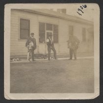 Three unidentified men outside a white house, with game birds