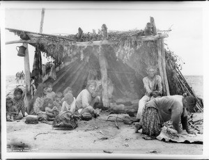 Navajo family in their hogan on the Painted Desert preparing a meal, showing view from front, ca.1901