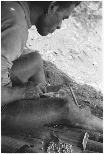 Man chipping shell money beads with blade