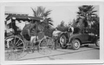 Horse-drawn carriage being towed by coupe with rumble seat