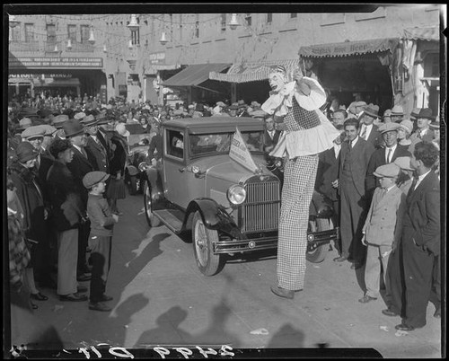 Clown on stilts, advertising dance marathon, with crowd and Essex car, Santa Monica, 1928