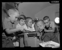 Children's books writer Edmund Lindop at a typewriter with his nieces and nephews crowding around him, 1961