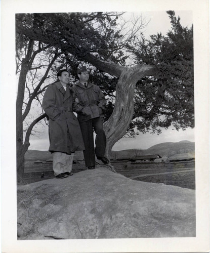 Two men posing with tree near village