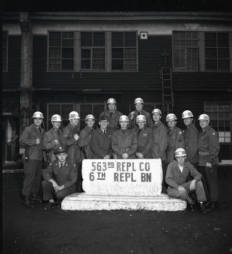 Group photo of soldiers with sign in front of barracks at Camp Drake in Japan