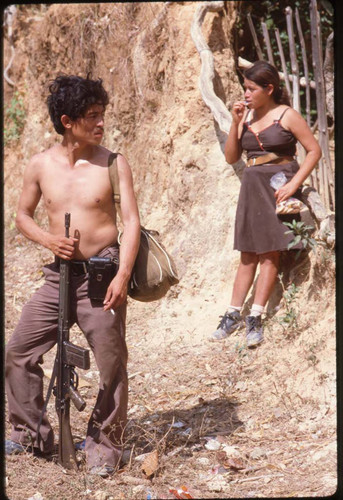 An armed guerrillero and a woman stand on an unpaved trail, La Palma, 1983